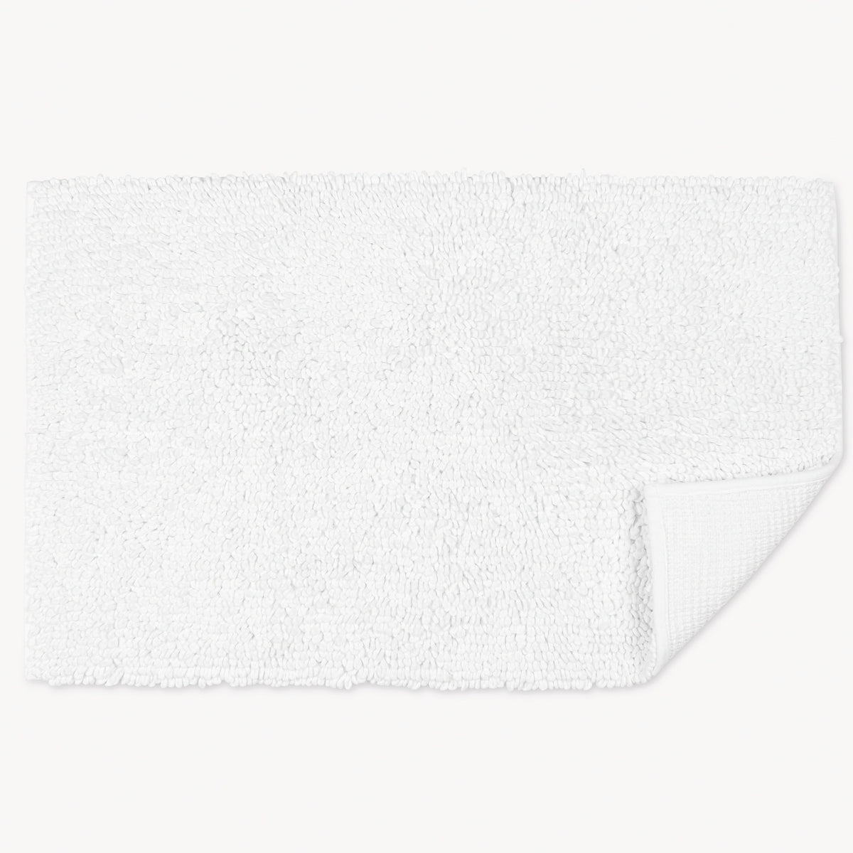 A rectangular white cotton bath rug with a textured surface and one corner slightly folded up.