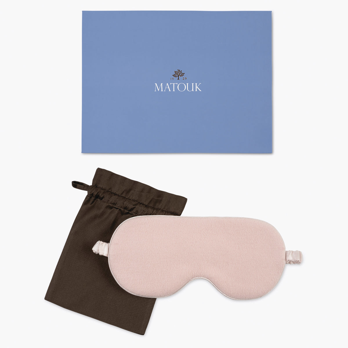Pink sleep mask with brown drawstring bag and blue Matouk branded box on a white background