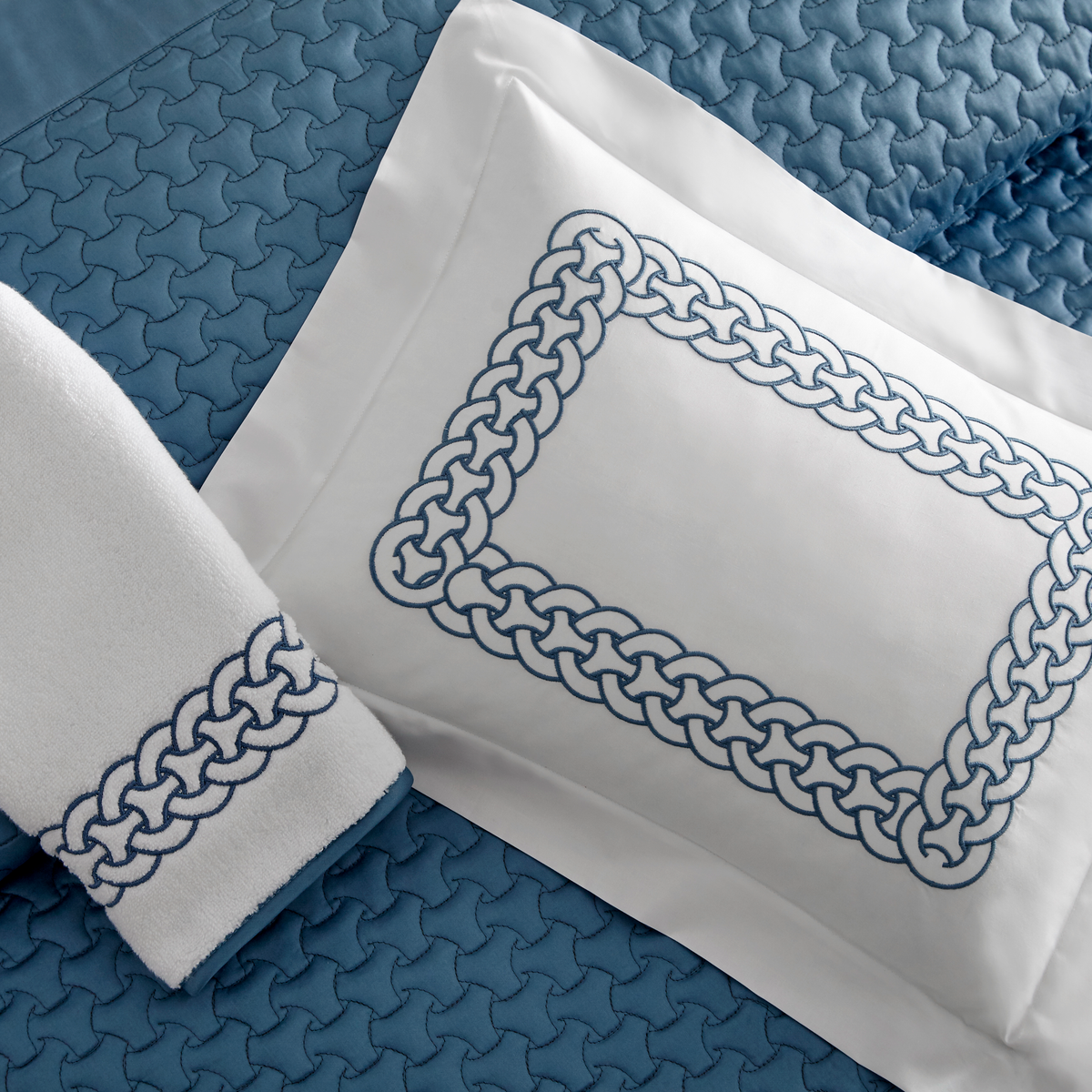 A white pillow with a blue chain-link border coordinates with Home Treasures Links Bedding on a blue quilted bedspread.