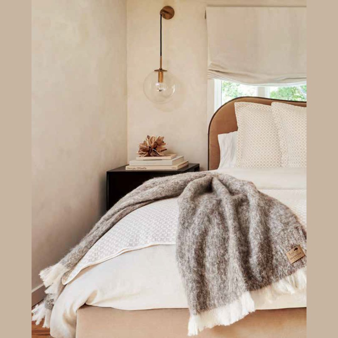 Cozy bedroom with a bed covered in a alpaca throw, books on a nightstand, and a lamp.