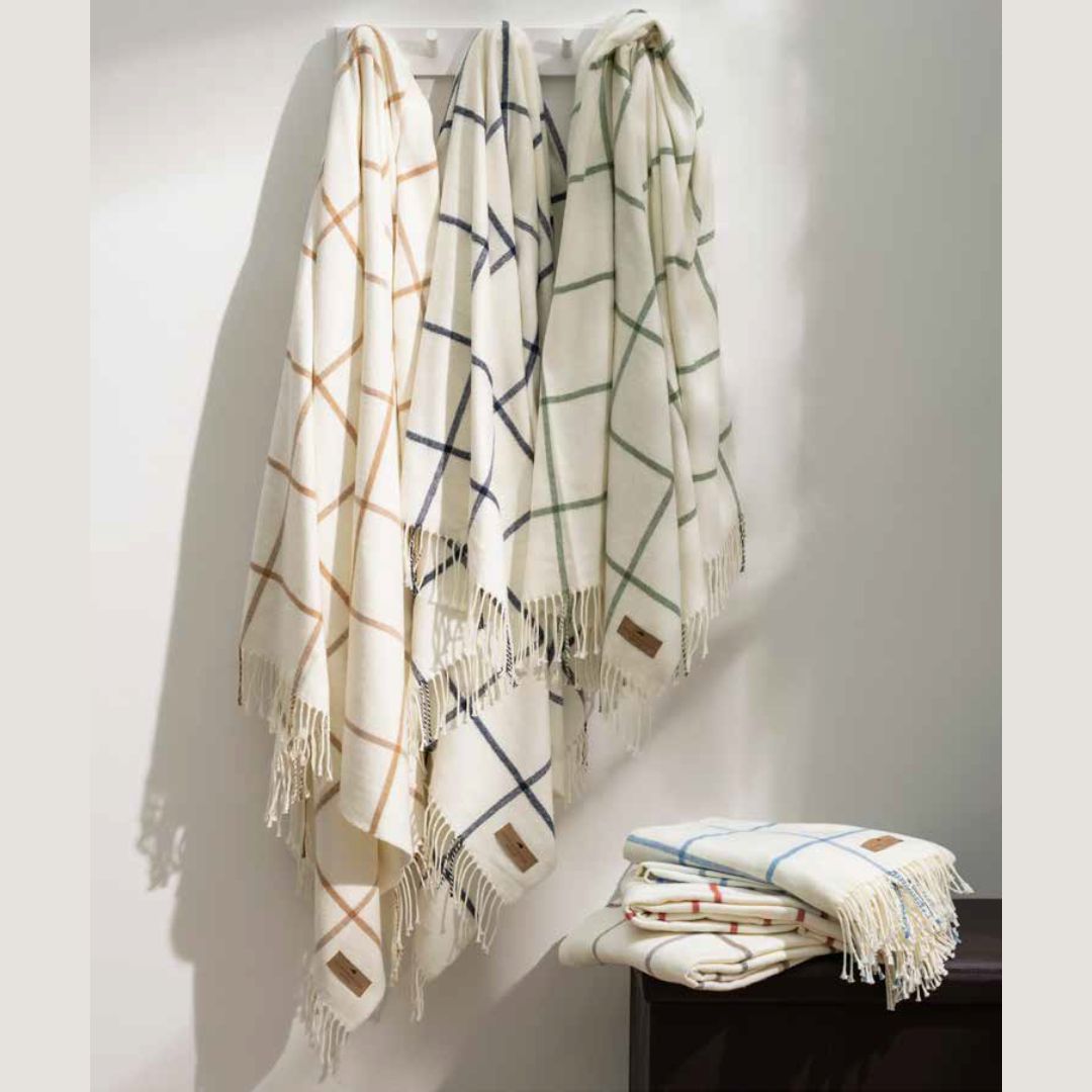 Four fringe Lands Downunder throws hang on hooks; two luxury throw blankets are folded on the table below.