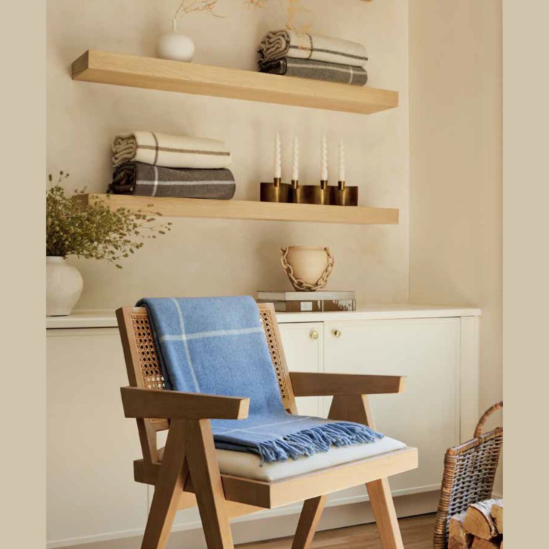 Wooden chair with a Lands Downunder Windowpane Cashmere Throw in Sky Blue draped over it, in front of a shelf with decorative items.