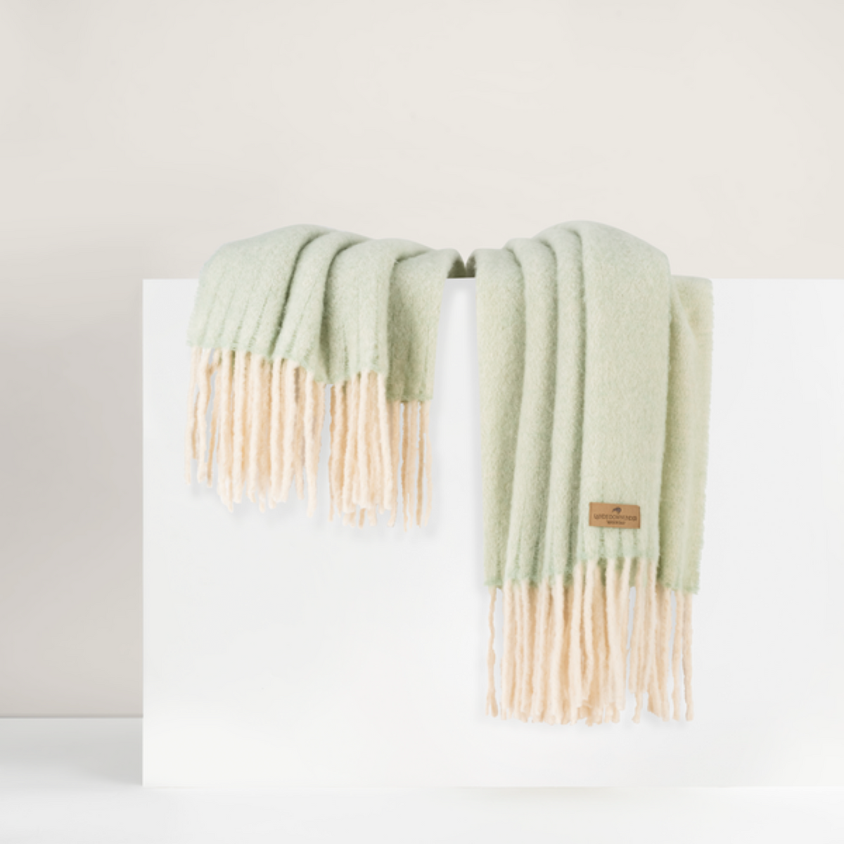 Lands Downunder Andes Throw, in Celadon color with fringe, is draped over a white surface