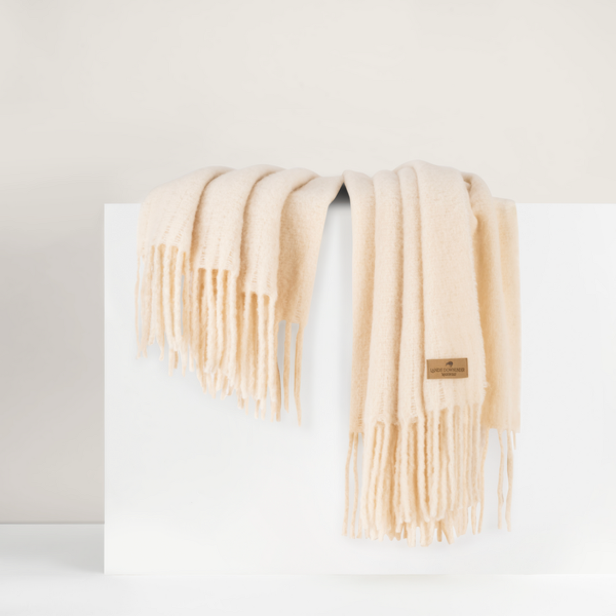 Lands Downunder Andes Throw, in Cream color with fringe, is draped over a white surface