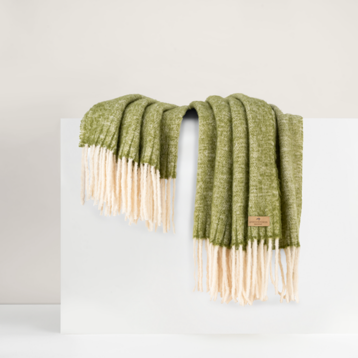 Lands Downunder Andes Throw, in Fern color with fringe, is draped over a white surface