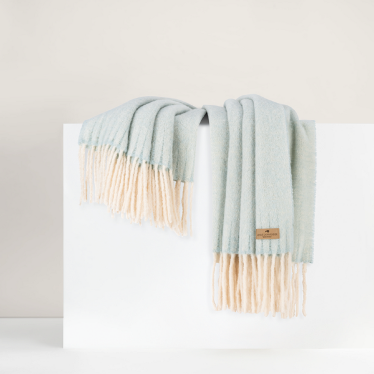 Lands Downunder Andes Throw, in Glacier color with fringe, is draped over a white surface