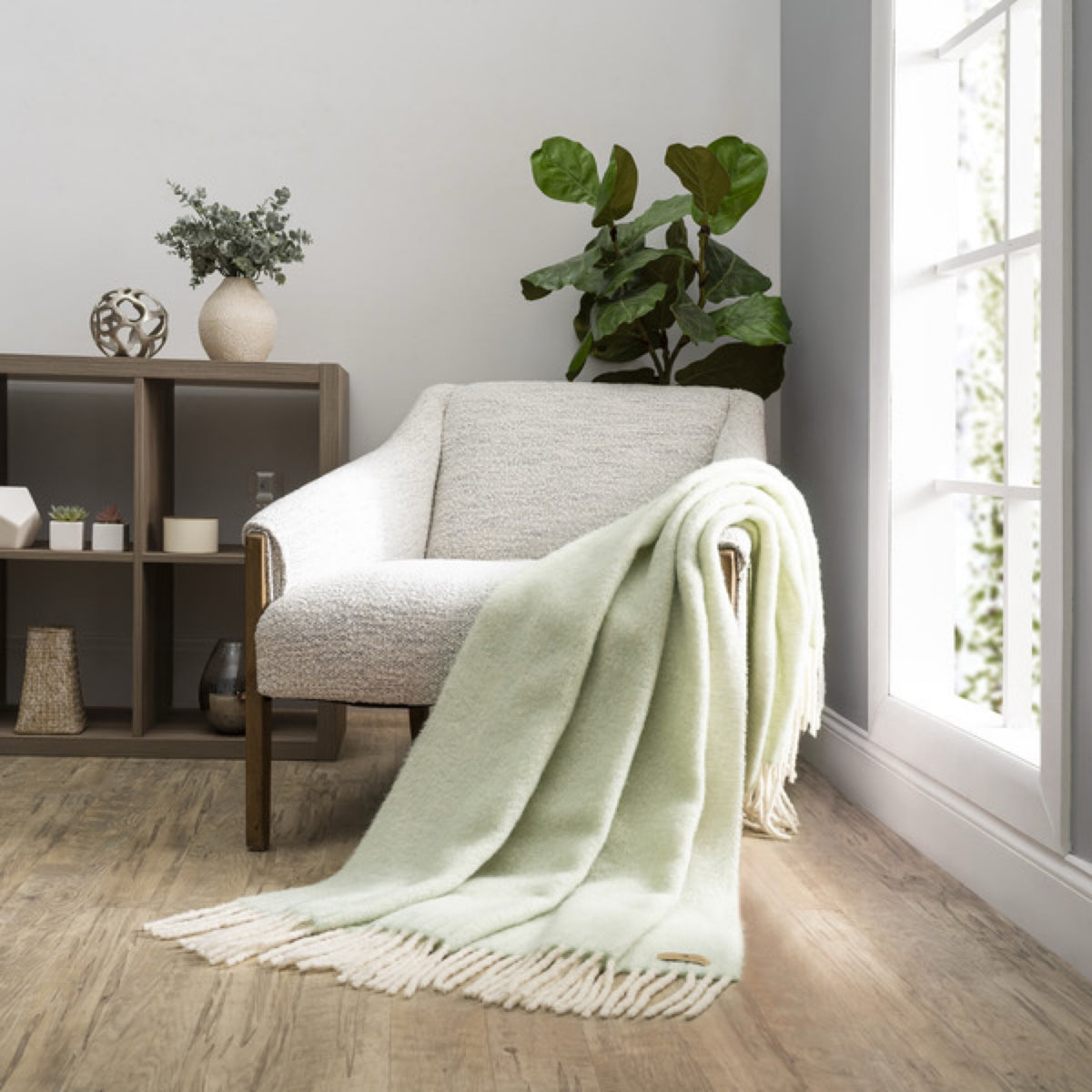 A Lands Downunder Andes Throw in Celadon color draped over a light armchair by a window adds cozy home decor