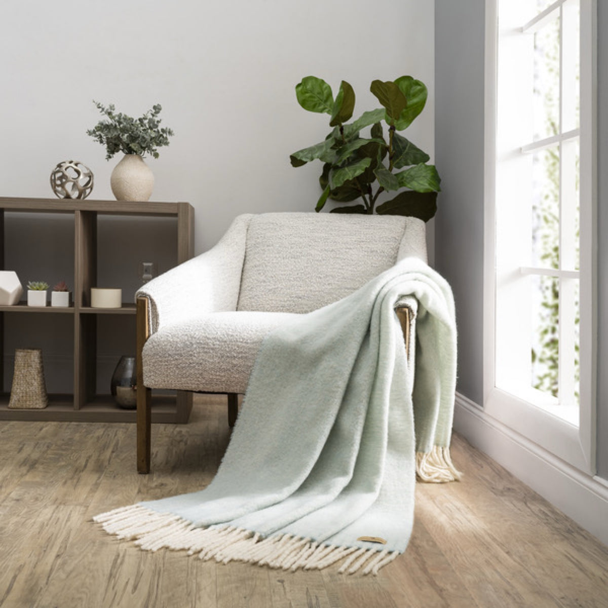 A Lands Downunder Andes Throw in Glacier color draped over a light armchair by a window adds cozy home decor