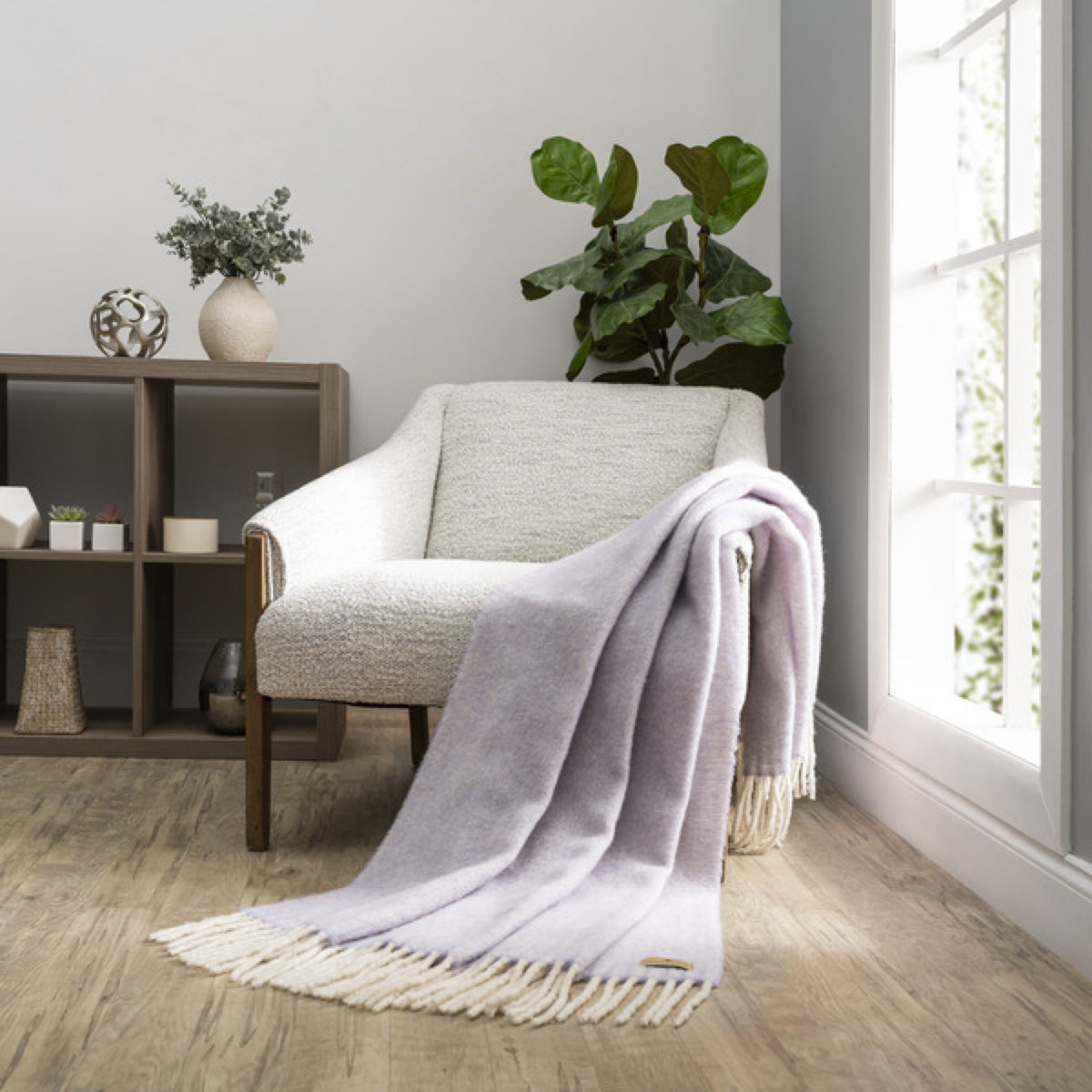 A Lands Downunder Andes Throw in Lavender color draped over a light armchair by a window adds cozy home decor