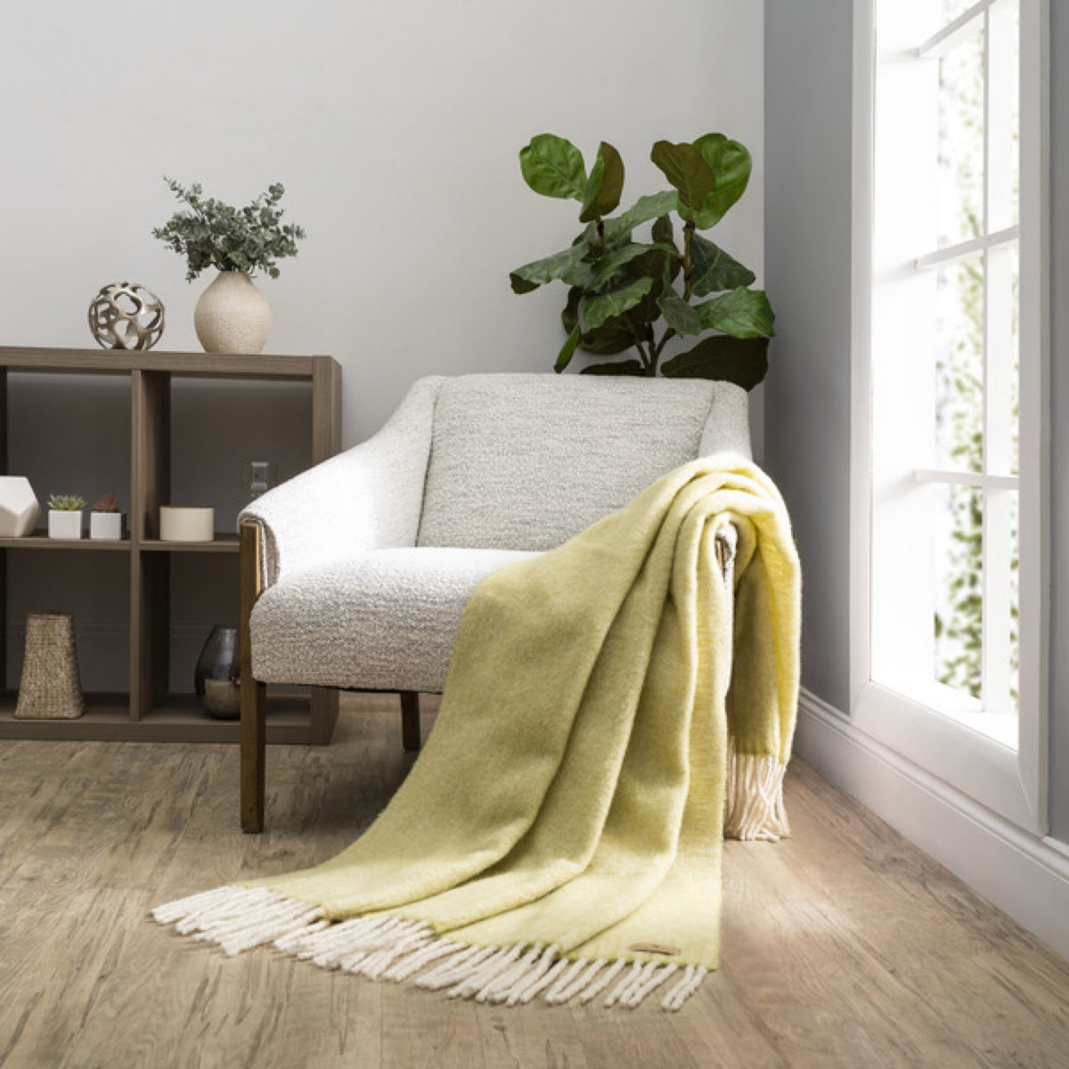 A Lands Downunder Andes Throw in Lemongrass color draped over a light armchair by a window adds cozy home decor