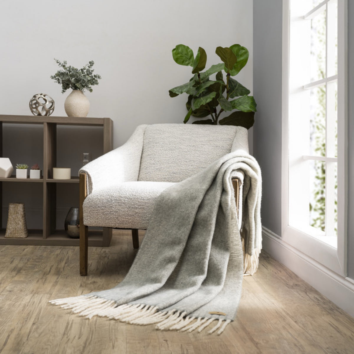 A Lands Downunder Andes Throw in Sterling color draped over a light armchair by a window adds cozy home decor