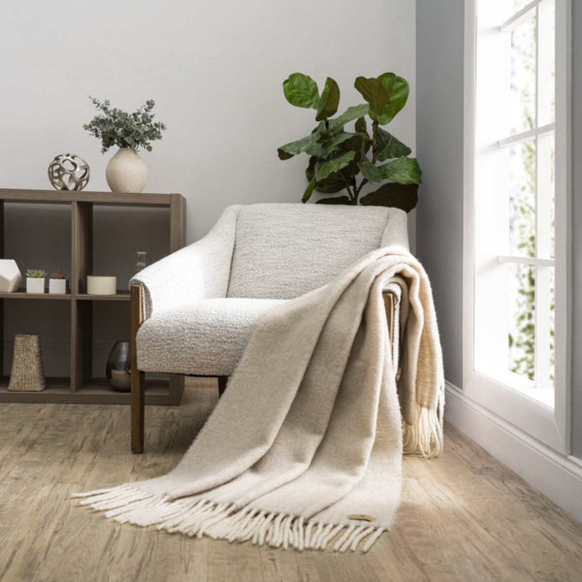 A Lands Downunder Andes Throw in Truffle color draped over a light armchair by a window adds cozy home decor