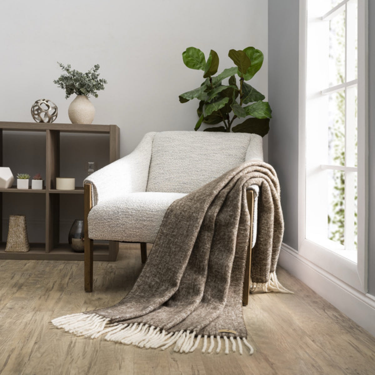 A Lands Downunder Andes Throw in Walnut color draped over a light armchair by a window adds cozy home decor