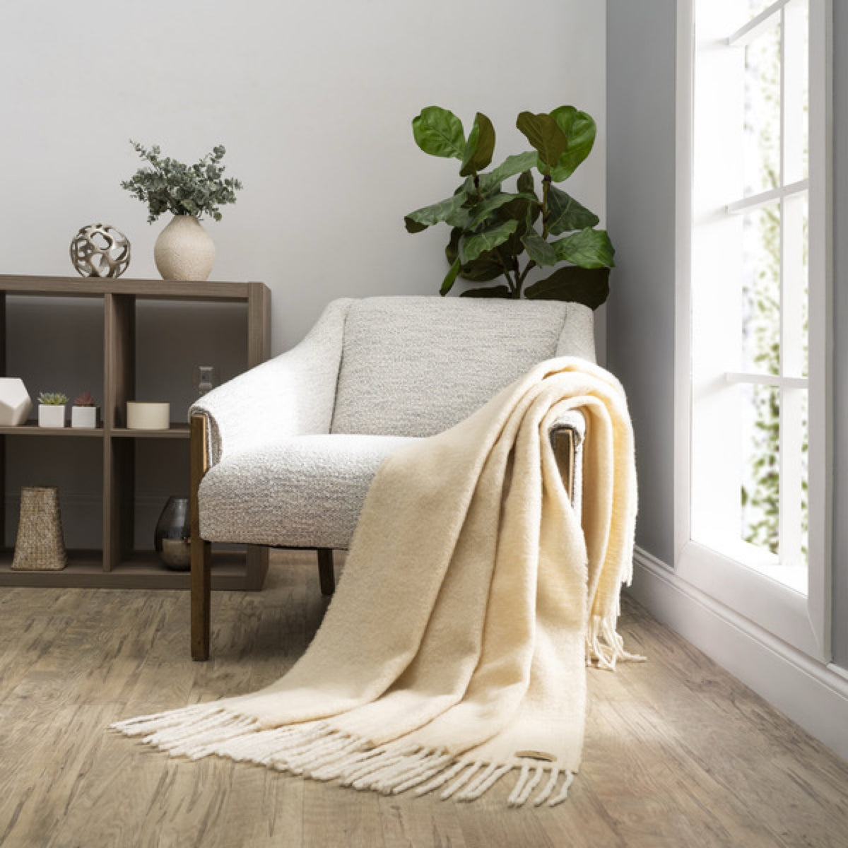 A Lands Downunder Andes Throw in Wheat color draped over a light armchair by a window adds cozy home decor