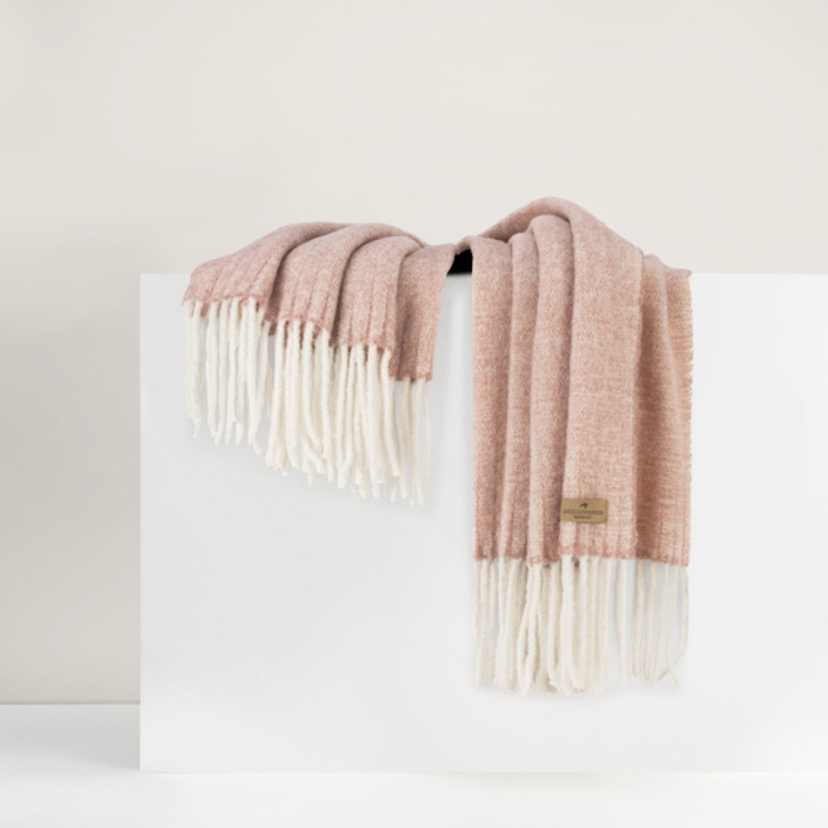 Lands Downunder Andes Throw, in Rose Quartz color with fringe, is draped over a white surface