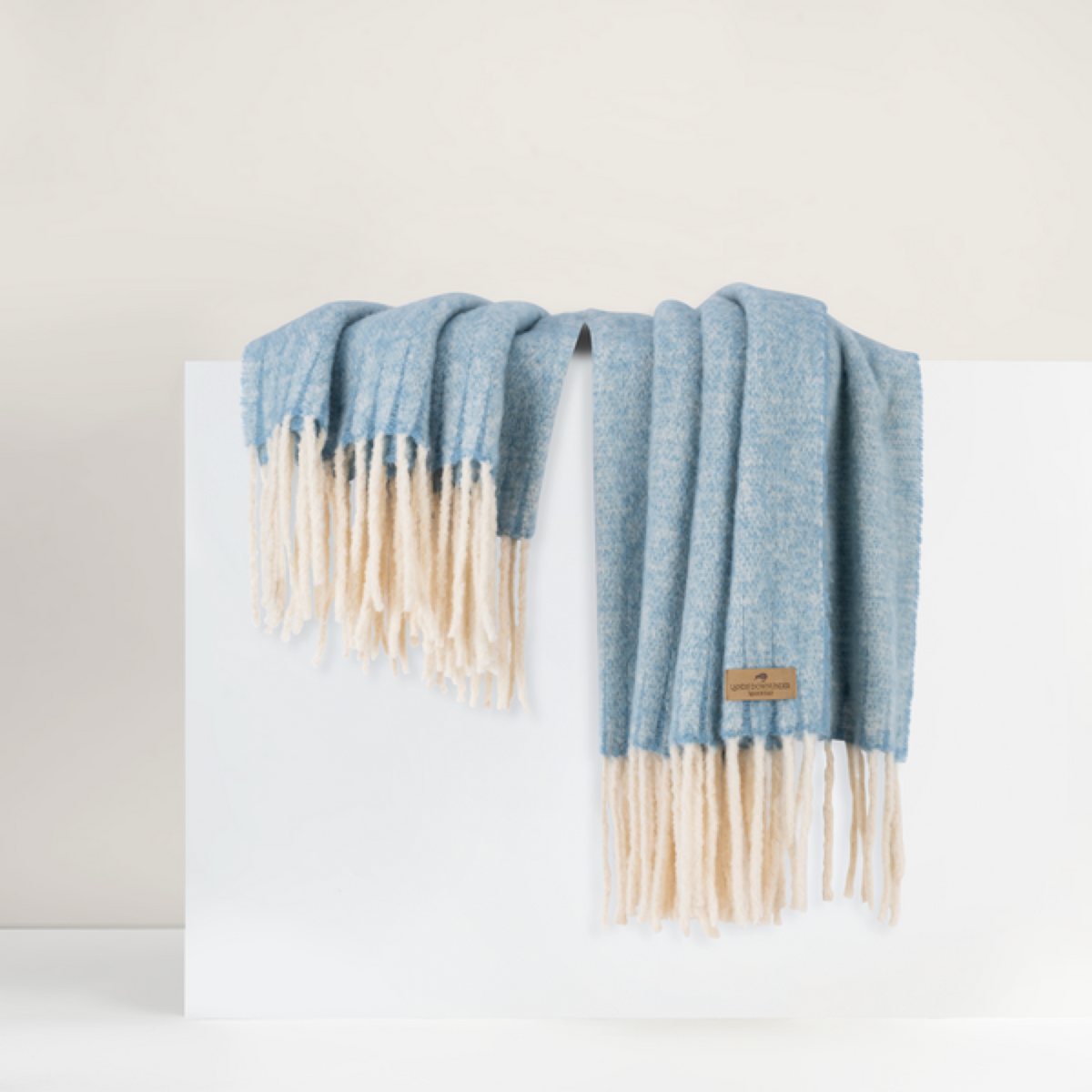 Lands Downunder Andes Throw, in Sky Blue color with fringe, is draped over a white surface