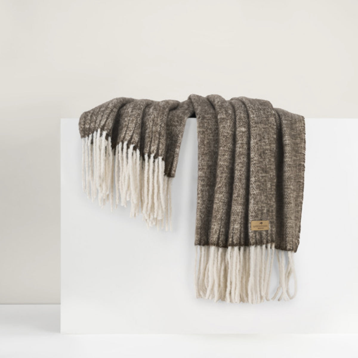 Lands Downunder Andes Throw, in Walnut color with fringe, is draped over a white surface