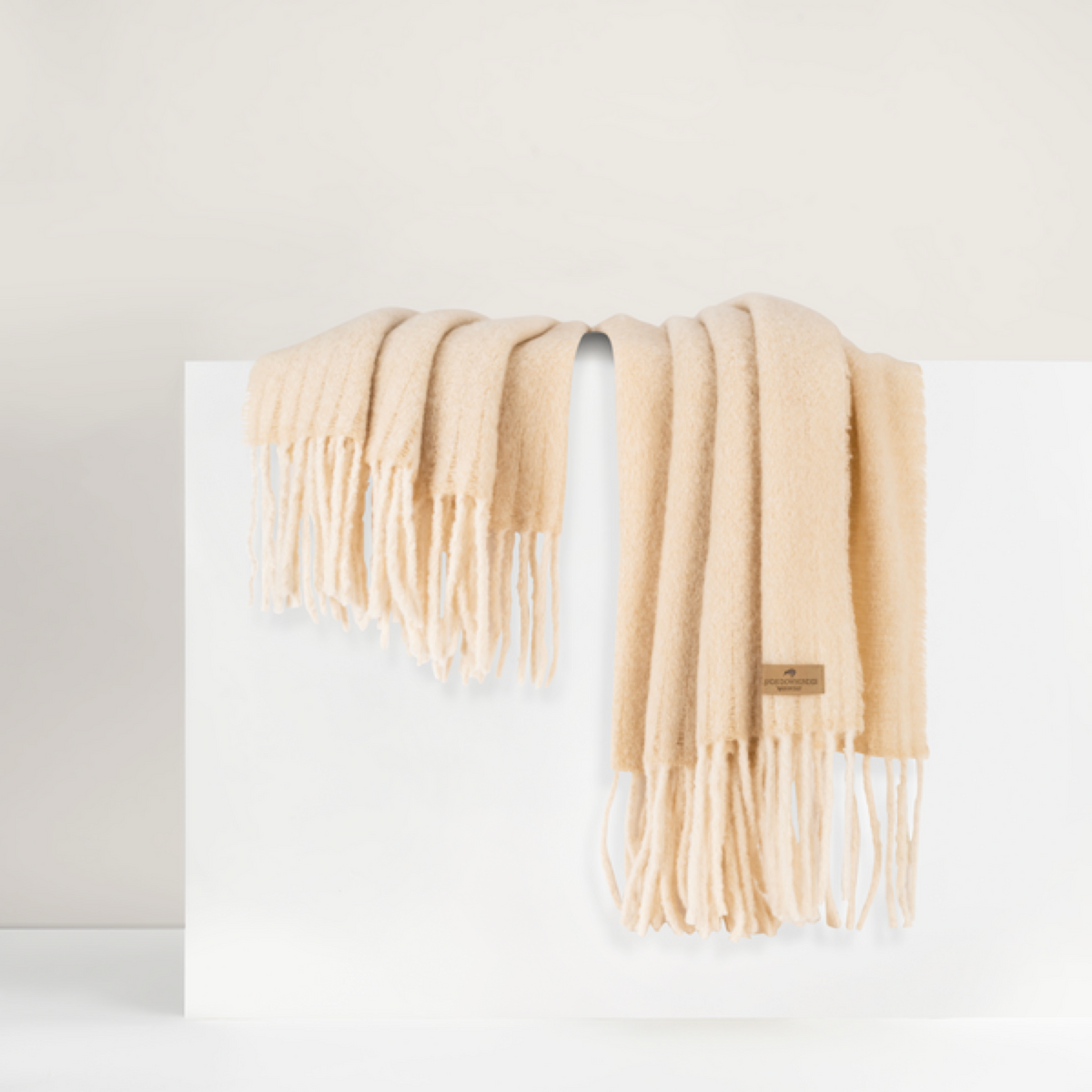 Lands Downunder Andes Throw, in Wheat color with fringe, is draped over a white surface