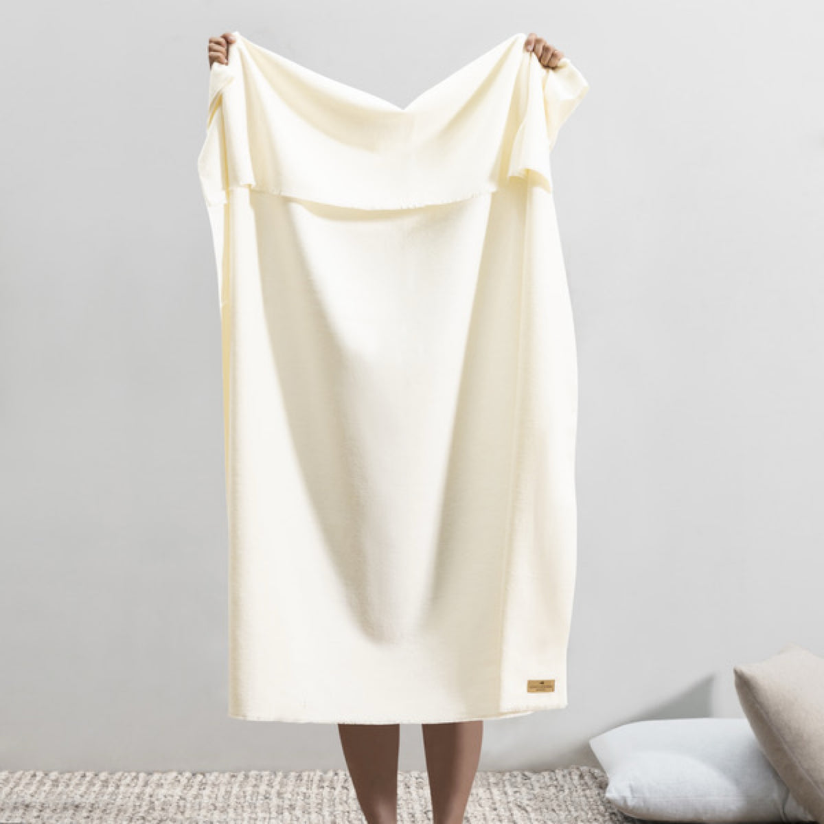 A person stands barefoot on a rug, holding up a Lands Downunder Aspen Peaks Throw in Snow color