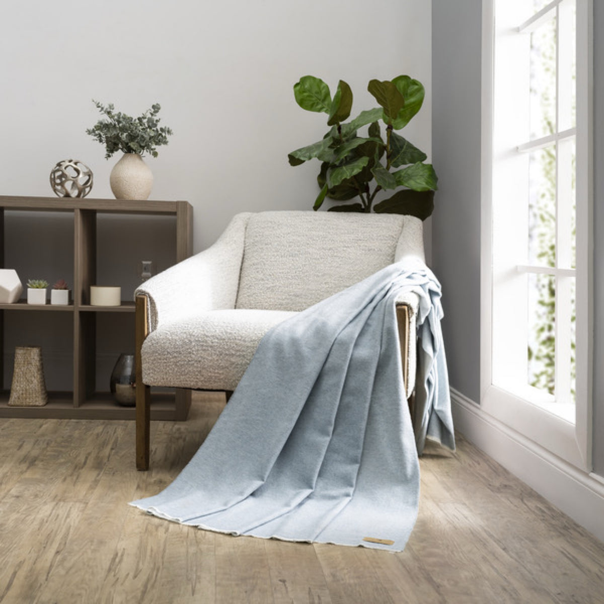 A Crystal Blue Lands Downunder Aspen Peaks Throw is draped over a cream armchair in a modern, minimalist living room