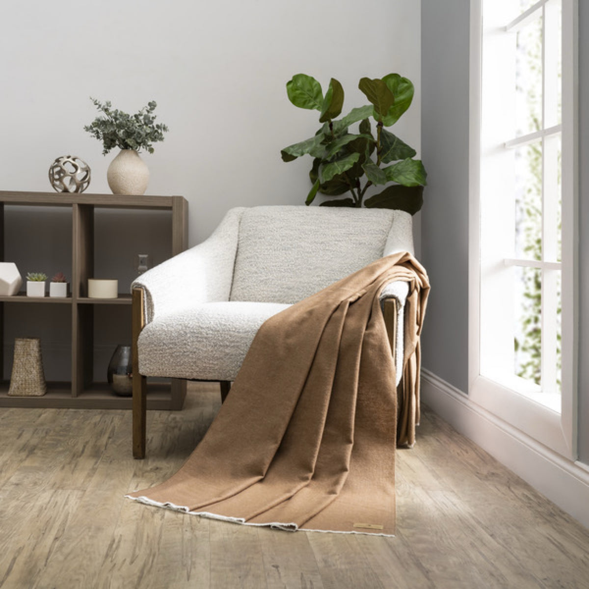 A Pinecone Lands Downunder Aspen Peaks Throw is draped over a cream armchair in a modern, minimalist living room