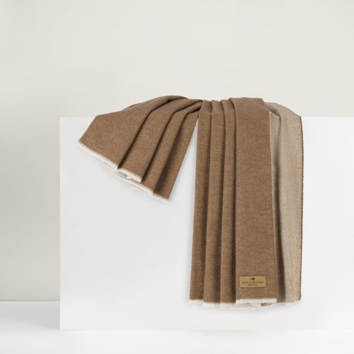 A brown wool scarf with a beige underside, like a luxury home accessory, draped over a white surface.