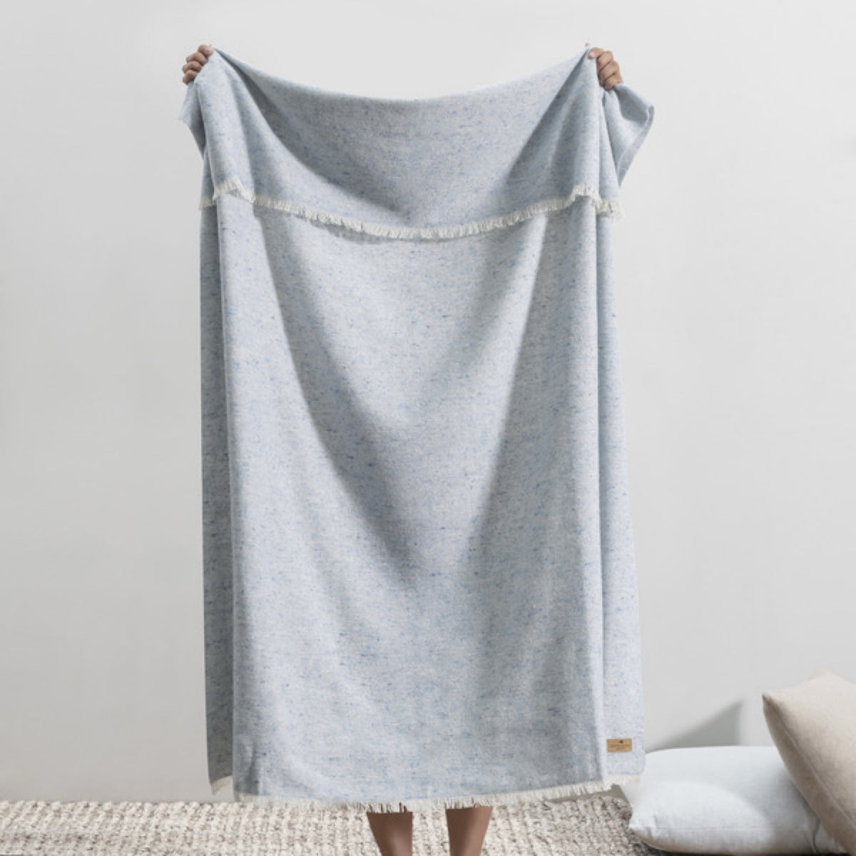 A person holds up a Lands Downunder Cinder Mist Throw in Crystal Blue color