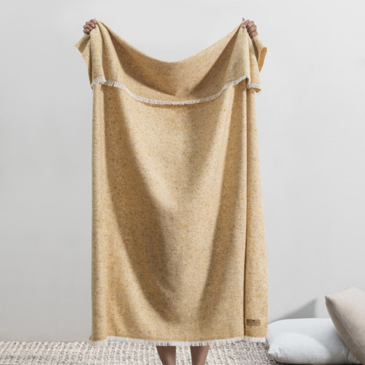 A person holds up a Lands Downunder Cinder Mist Throw in Gold color