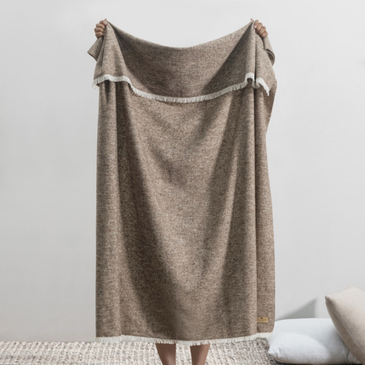 A person holds up a Lands Downunder Cinder Mist Throw in Mocha color