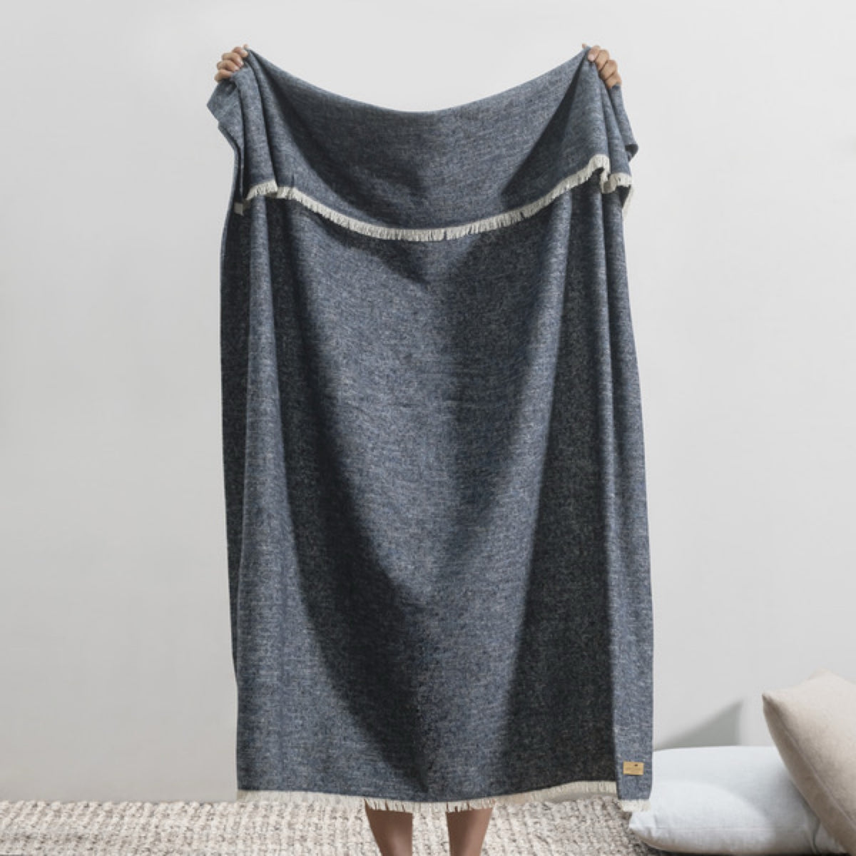 A person holds up a Lands Downunder Cinder Mist Throw in Navy color