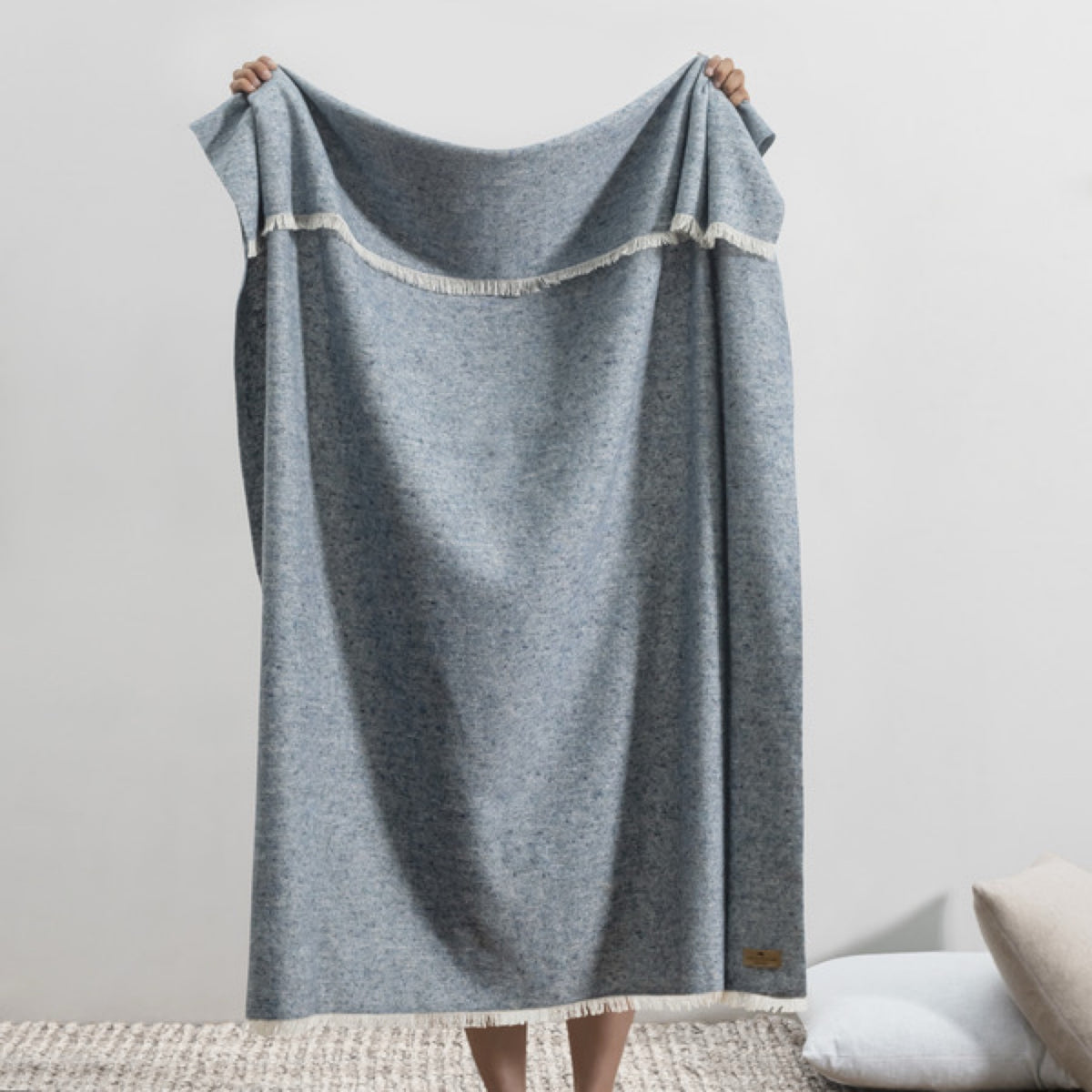 A person holds up a Lands Downunder Cinder Mist Throw in Ocean color