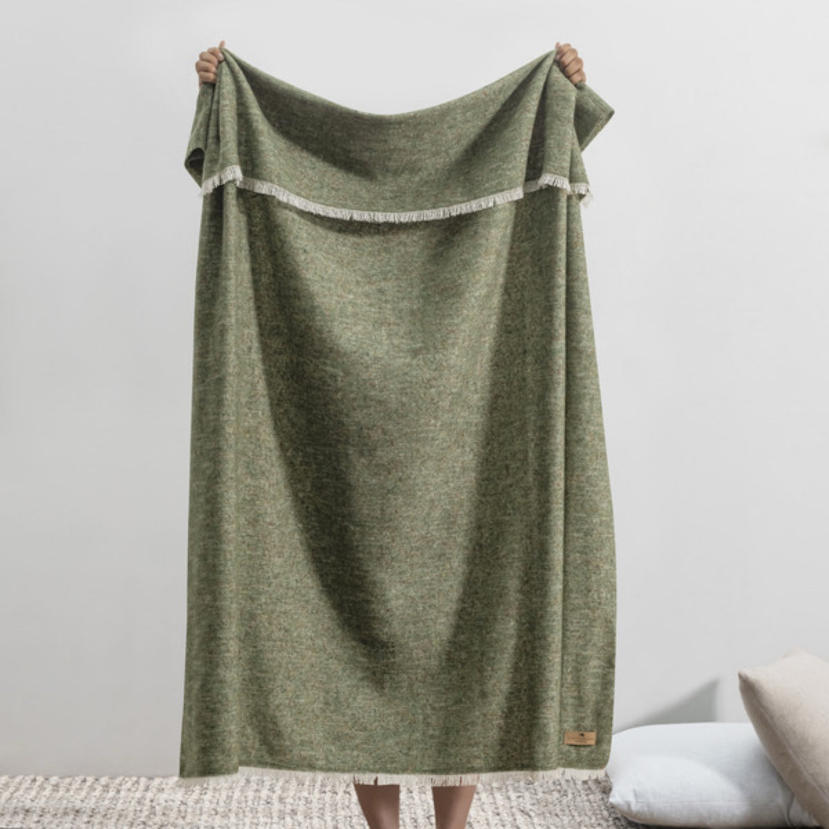 A person holds up a Lands Downunder Cinder Mist Throw in Olive color