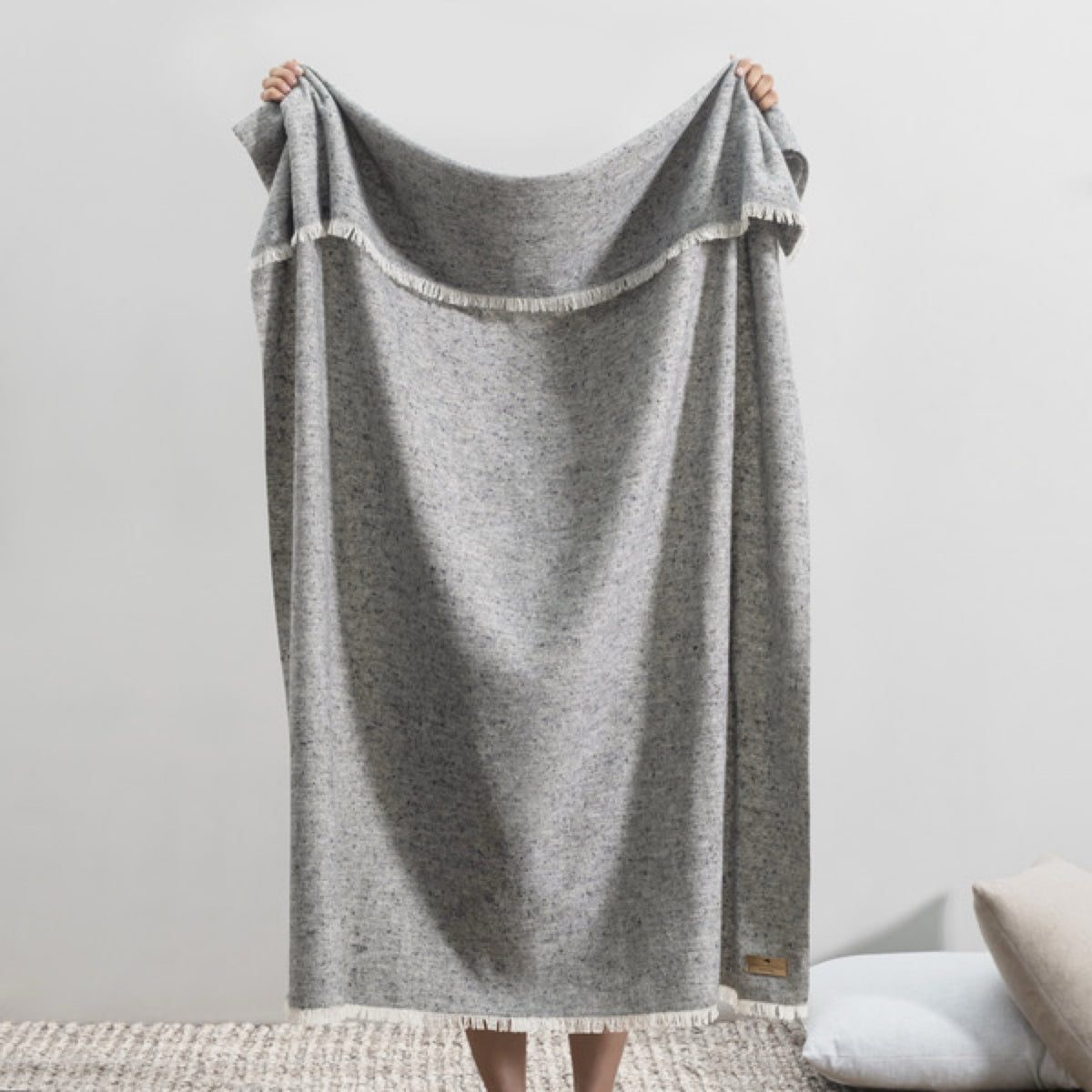 A person holds up a Lands Downunder Cinder Mist Throw in Stone color
