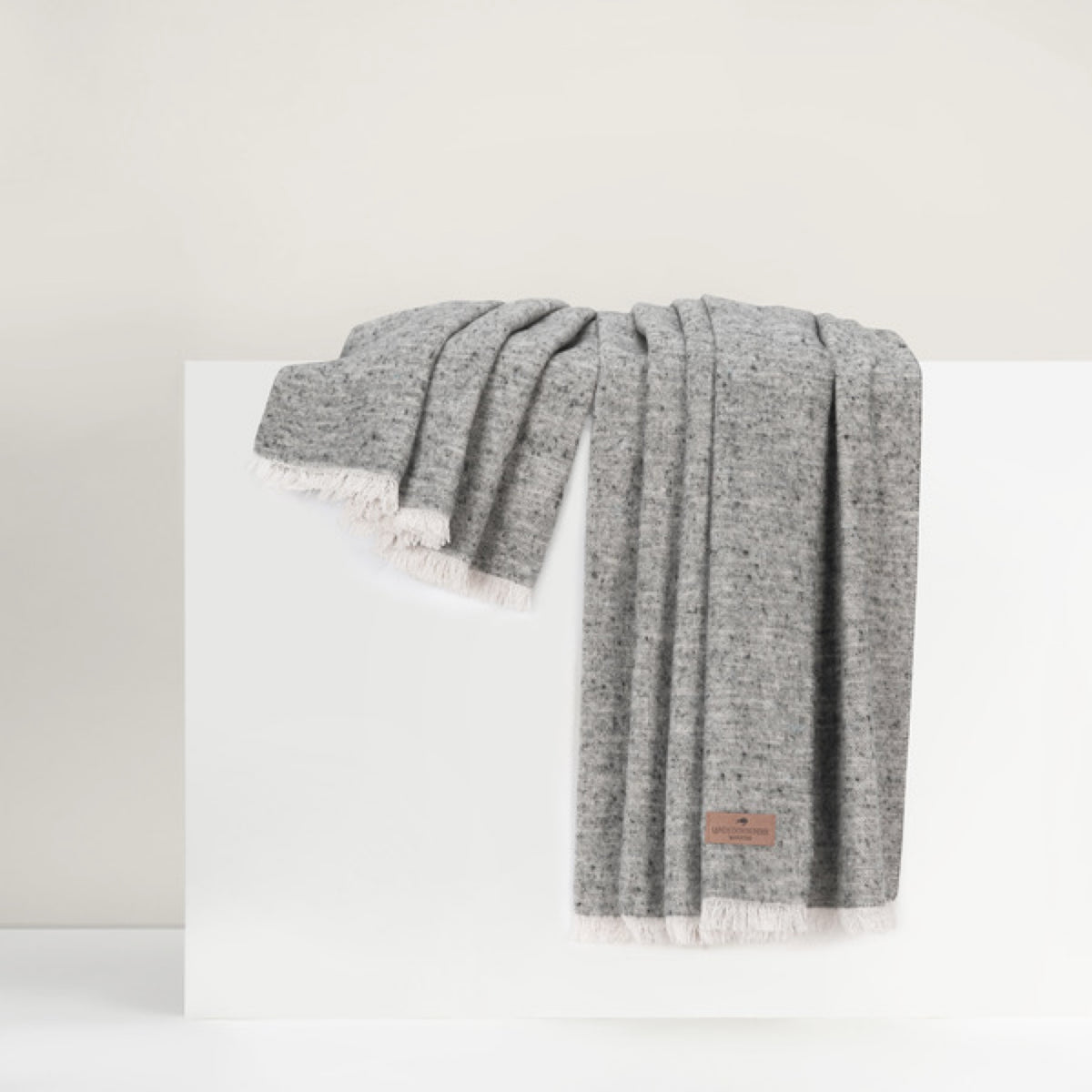 Lands Downunder Cinder Mist Throw in Stone color with fringed edges is draped over a white surface against a neutral background