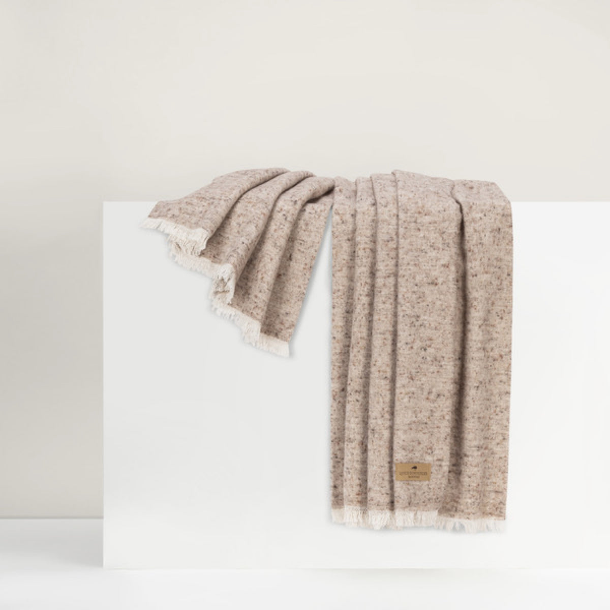 Lands Downunder Cinder Mist Throw in Taupe color with fringed edges is draped over a white surface against a neutral background