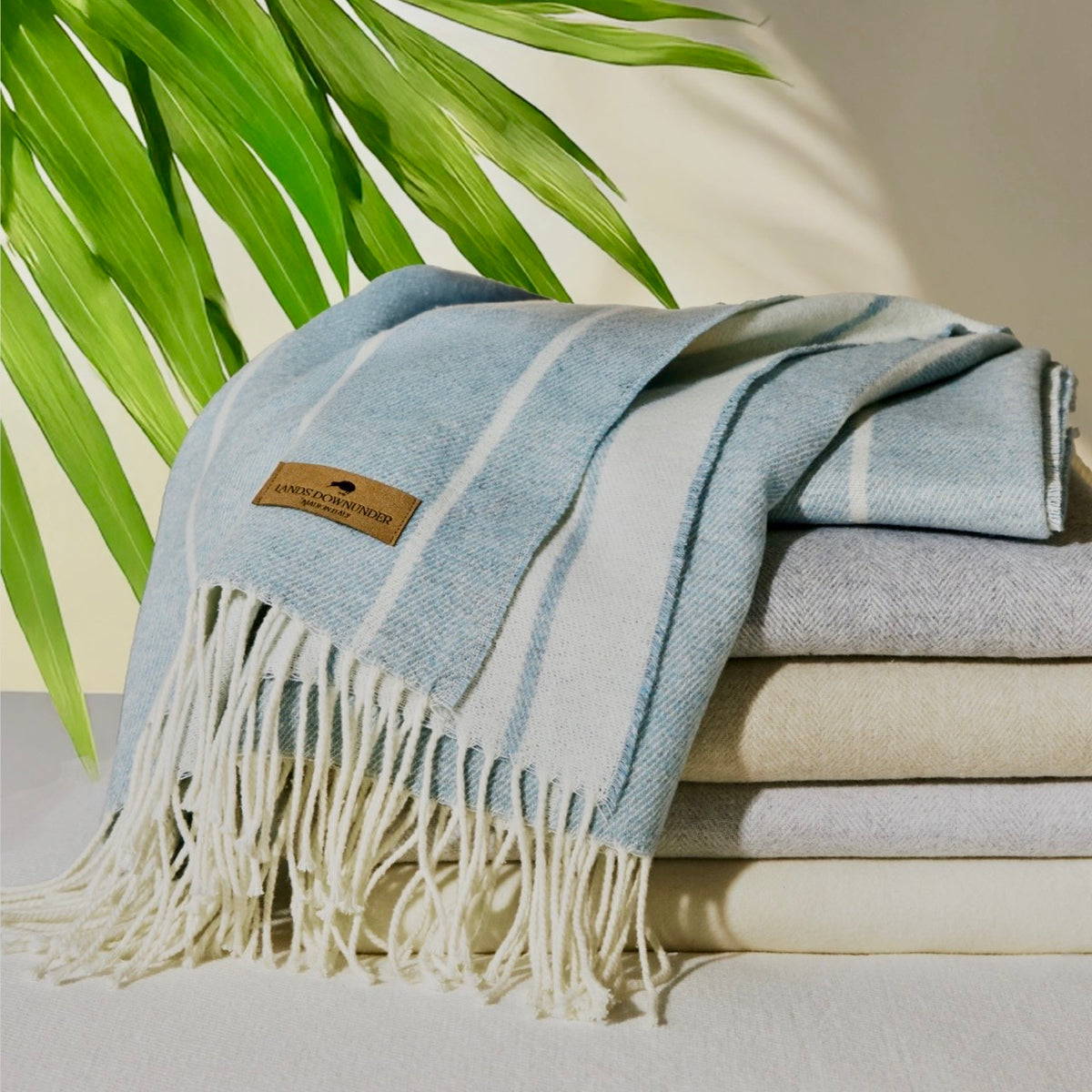 Stack of folded Lands Downunder Fiji Stripe Throws with greenery in the background