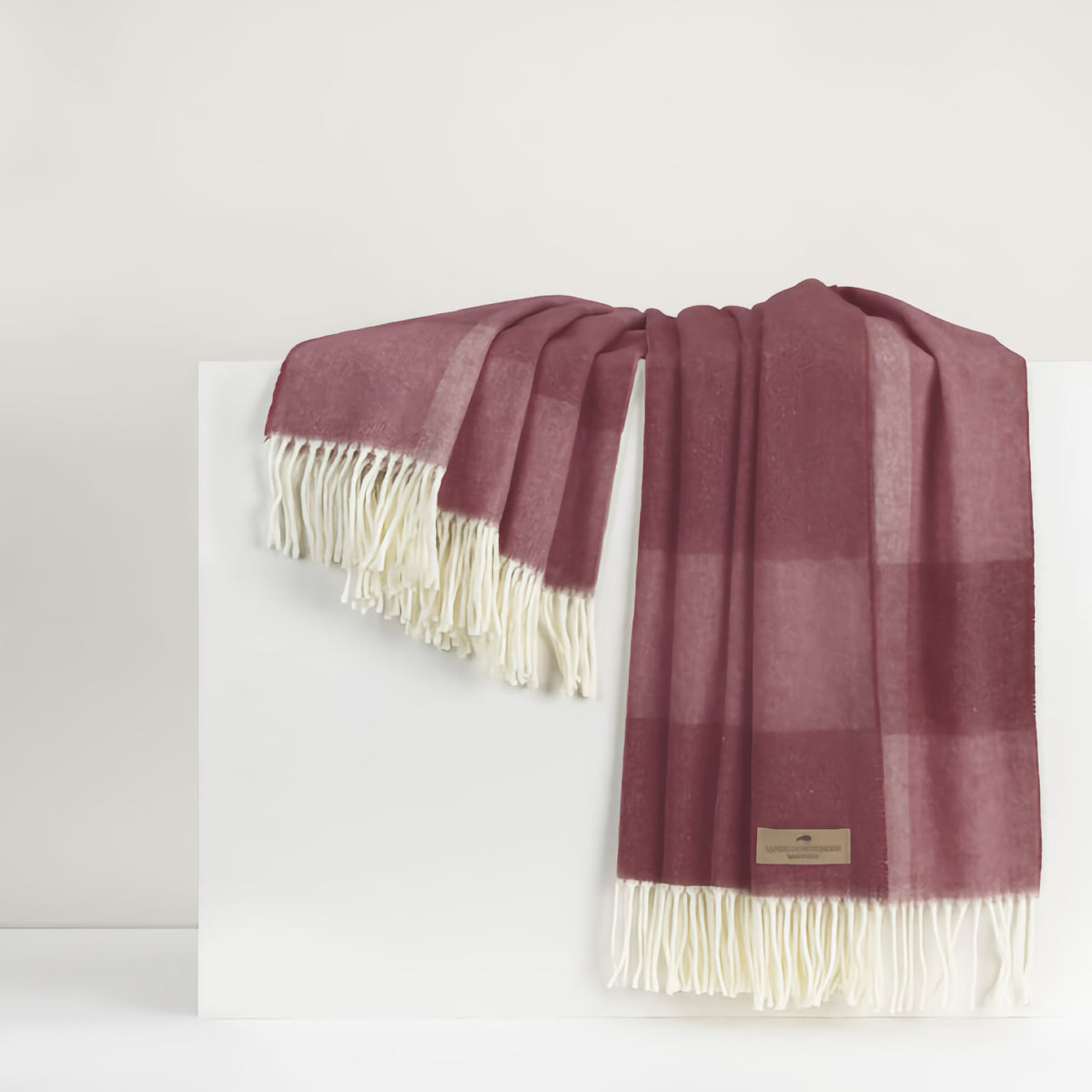 A luxury cotton acrylic throw with red plaid and white fringe draped over a white surface against a neutral background.