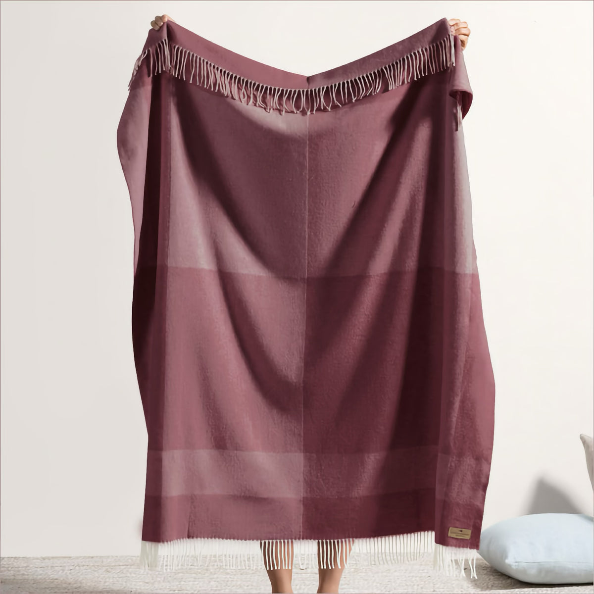 Person holding a luxury cotton acrylic throw in maroon with a subtle plaid pattern against a plain light background.