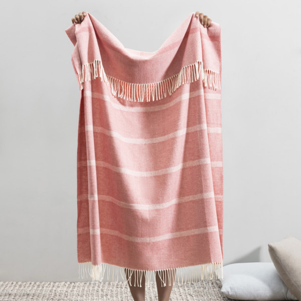 A person displays the Back Lands Downunder Montauk Stripe Herringbone Throws in Berry Sorbet color, against a plain backdrop