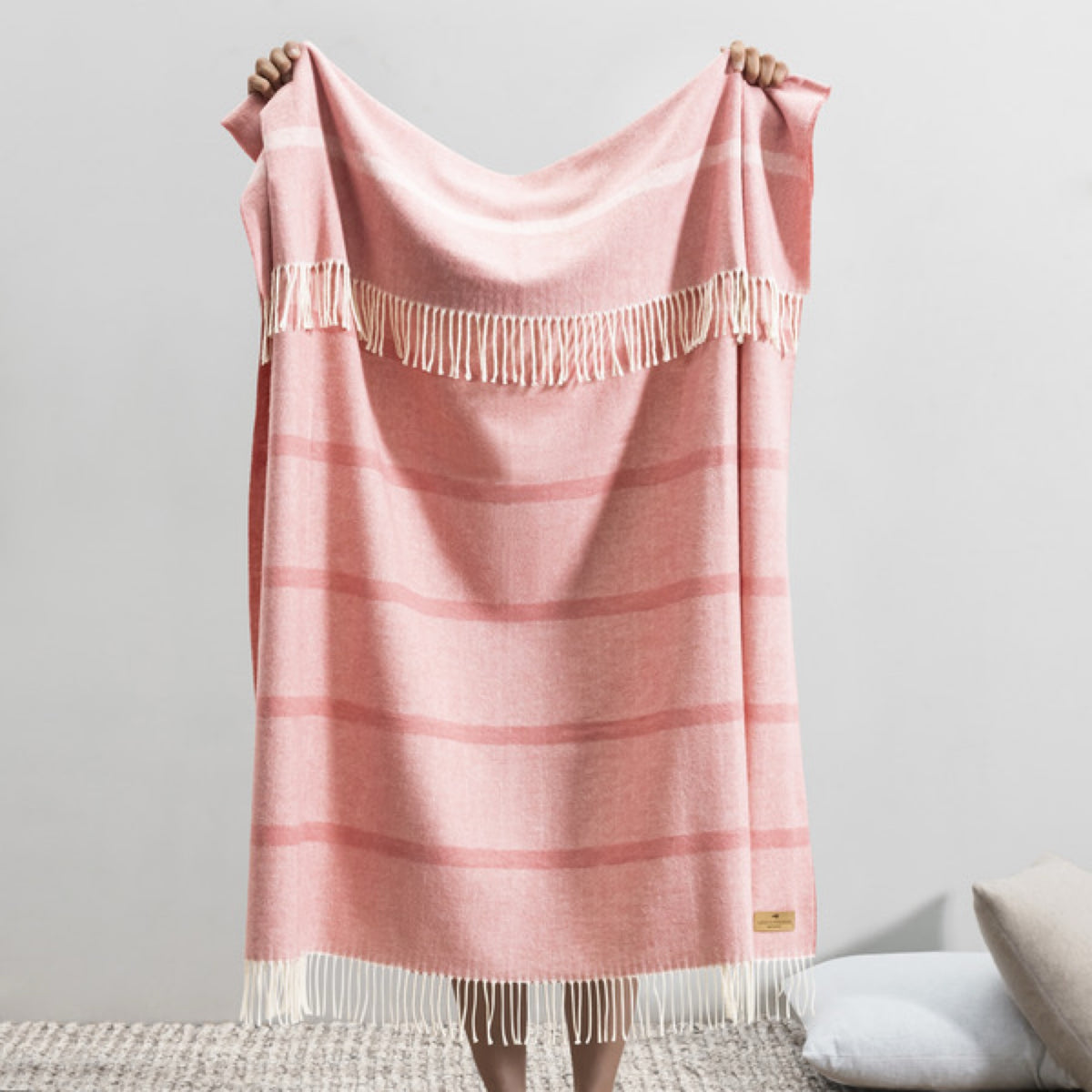 A person displays the front Lands Downunder Montauk Stripe Herringbone Throws in Berry Sorbet color, against a plain backdrop