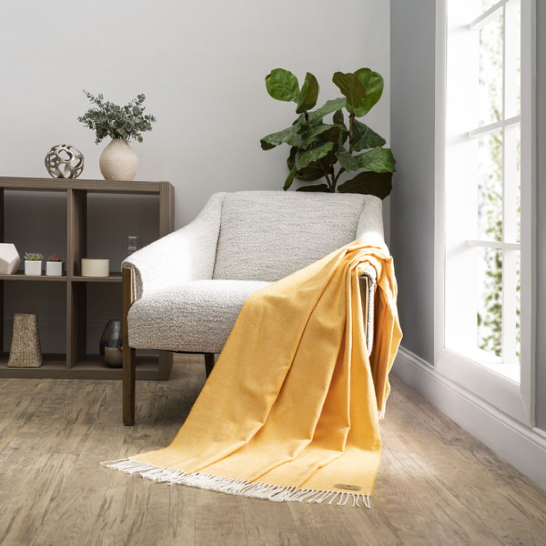 Yellow blanket draped over a gray armchair in a room with a bookshelf and plants.