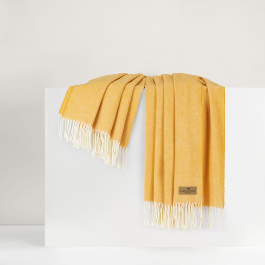 Mustard yellow throw blanket with white fringes on a white background
