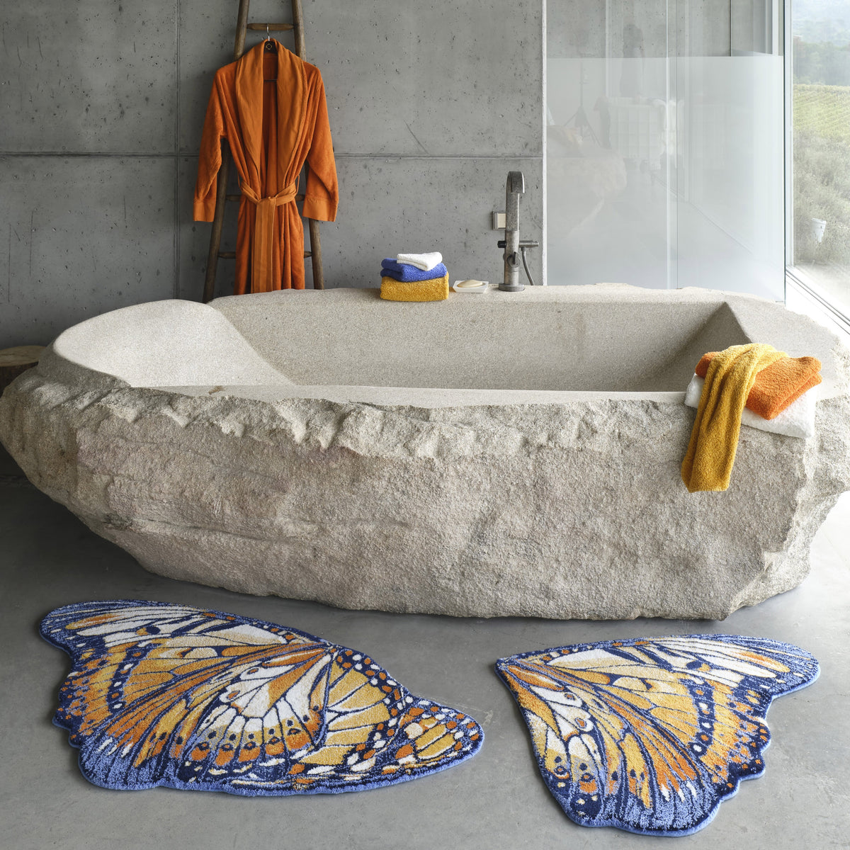 A stone bathtub with a towel, an Abyss Habidecor Mariposa Bath Rug, and a robe hanging on a wooden ladder.