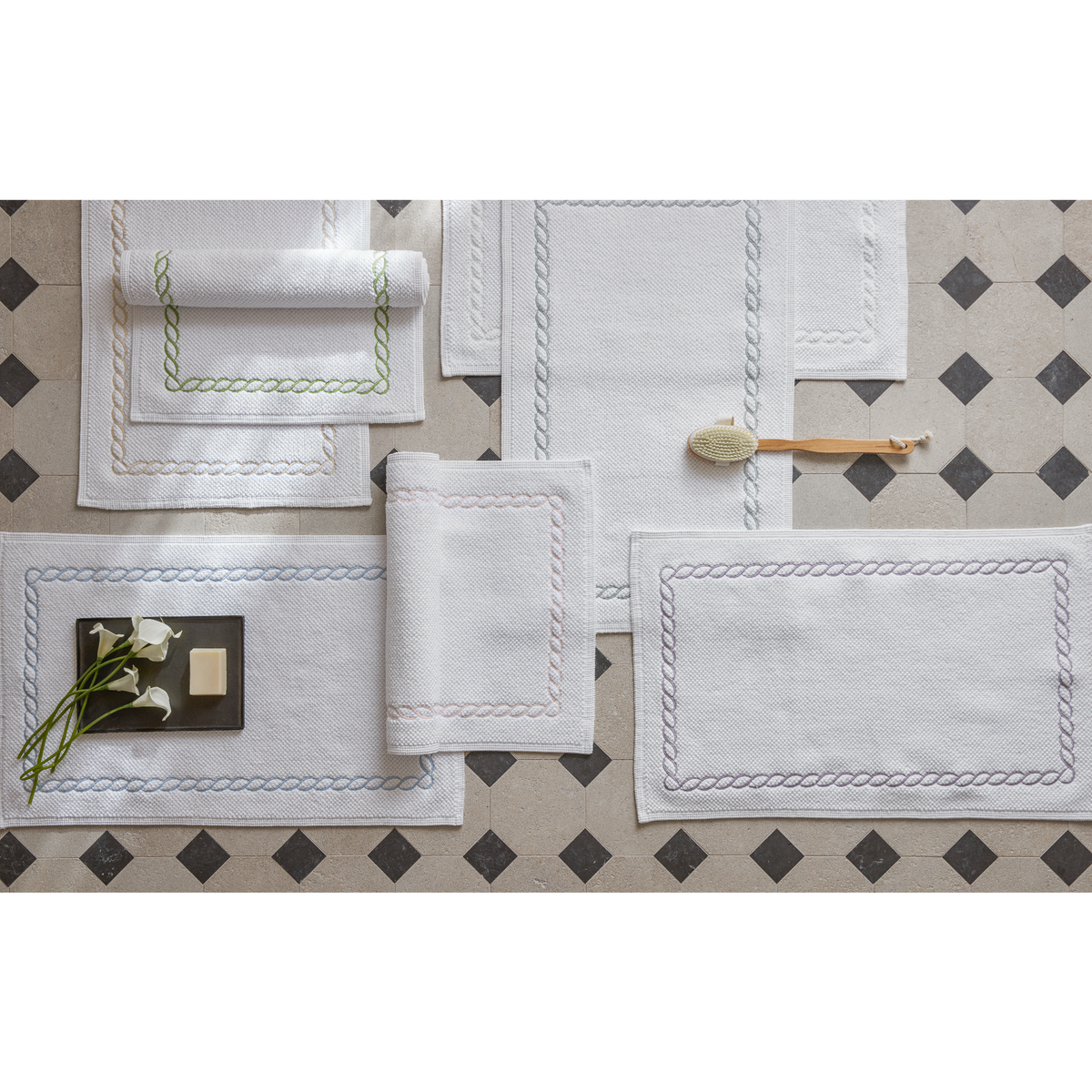 Several white Cairo long-staple cotton mats with Matouk Classic Chain borders are arranged on a tiled floor.