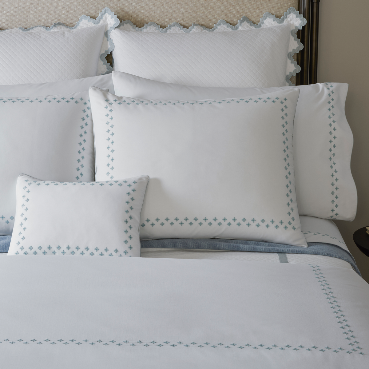 White bedding set with Pool Moroccan embroidery, including pillows and a duvet, neatly arranged on a bed.