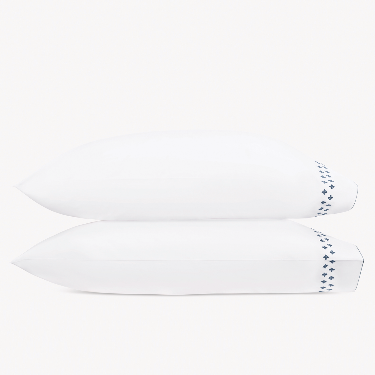 Two white pillows stacked horizontally feature Matouk Casablanca Embroidery in Indigo color
