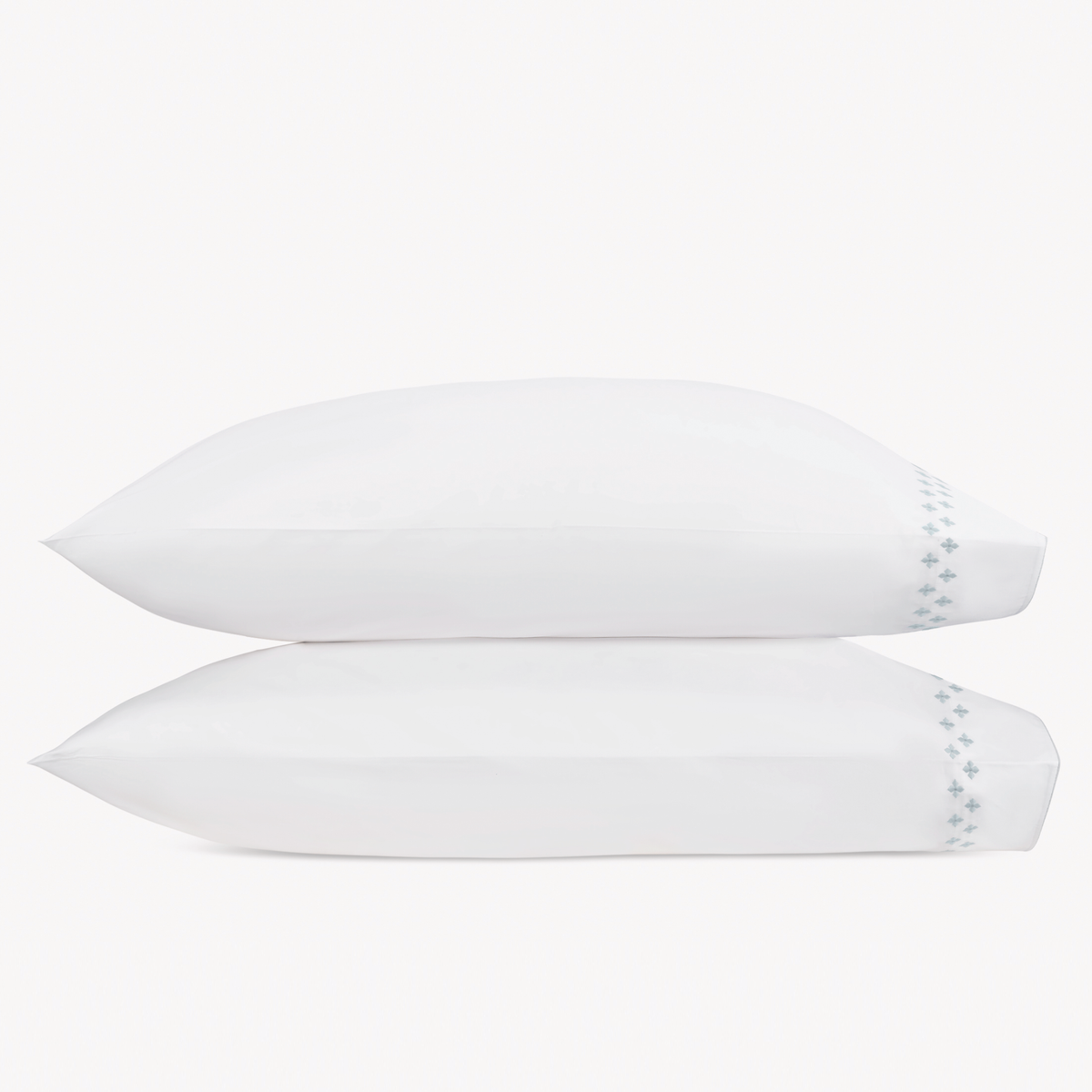 Two white pillows stacked horizontally feature Matouk Casablanca Embroidery in Pool color