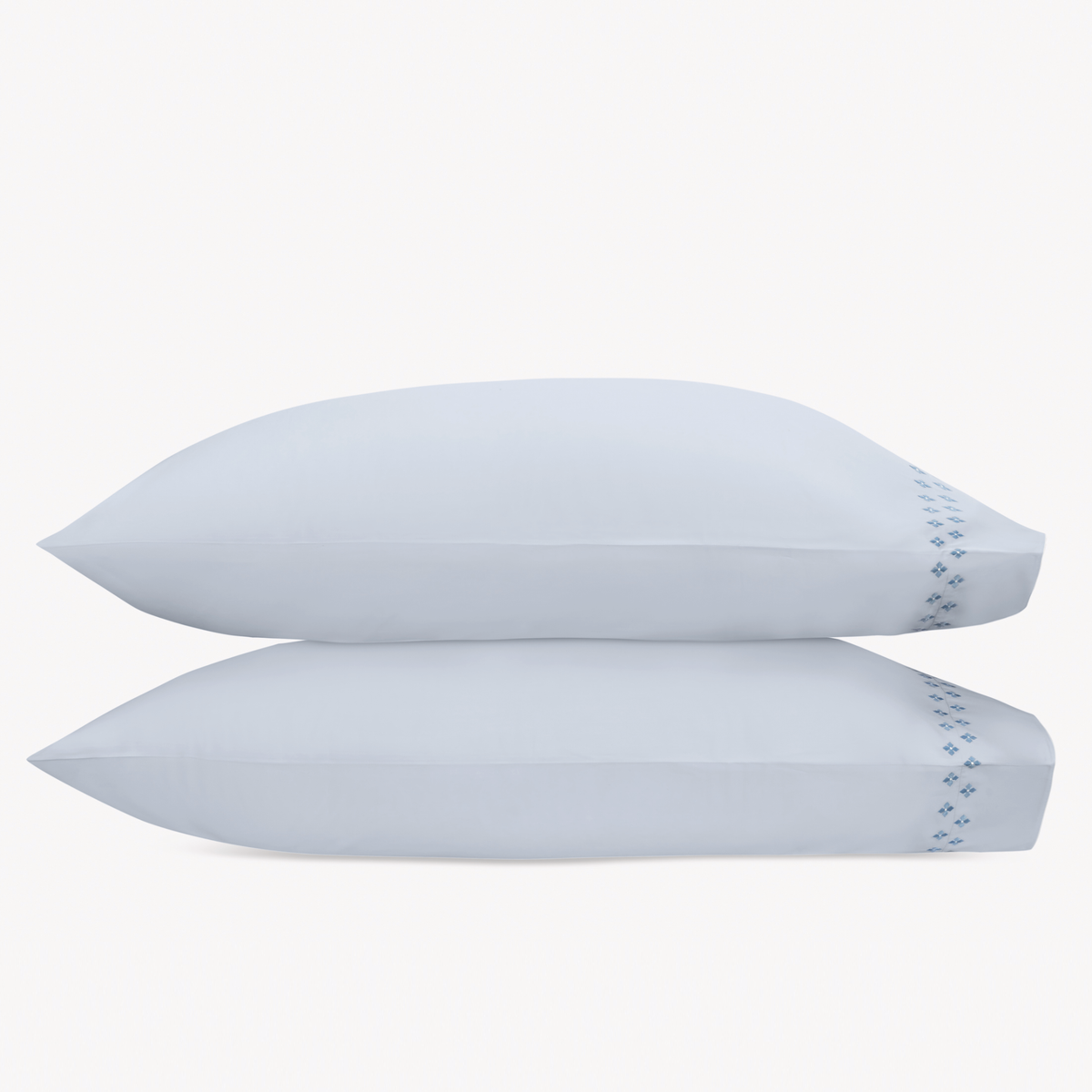 Two white pillows stacked horizontally feature Matouk Casablanca Embroidery in Sky Blue color