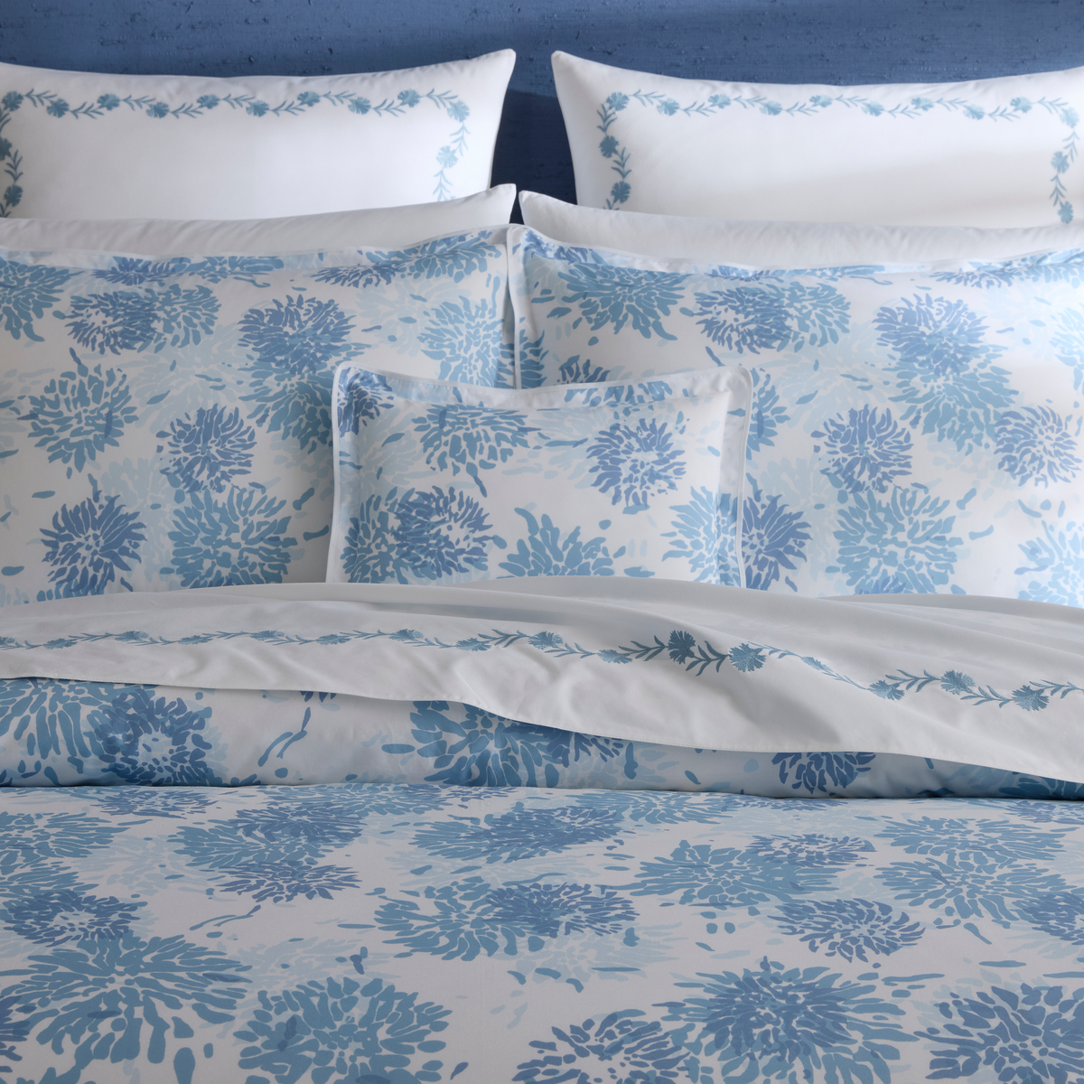 Closeup of a neatly made bed with Blue Matouk Chrysanthemum luxury bedding