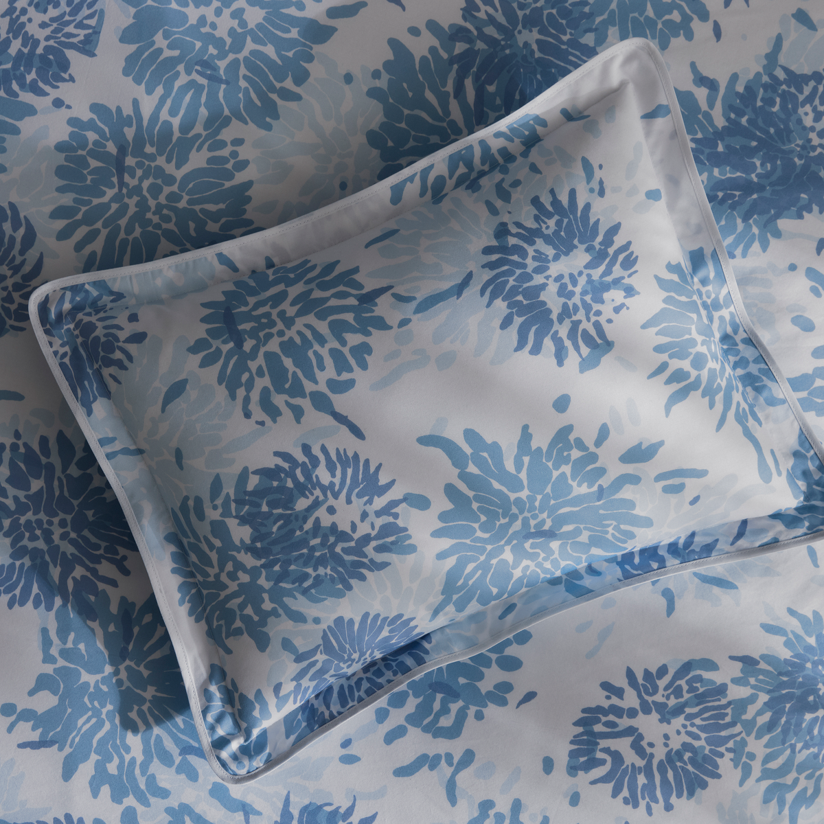 A pillow with a blue floral pattern from Matouk Chrysanthemum luxury bedding collection
